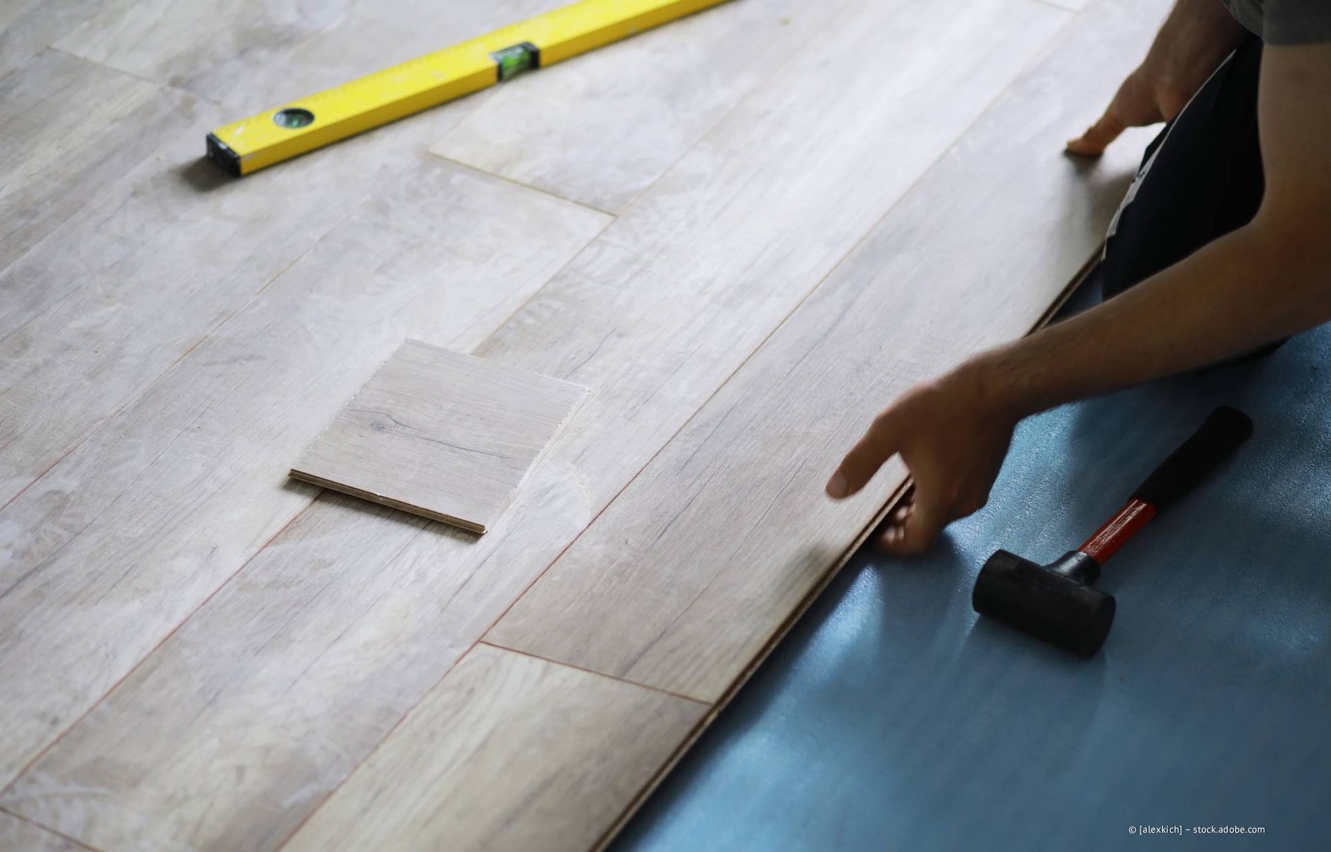 Eine Person verlegt mit Wasserwaage und Hammer helle Holzfußböden.