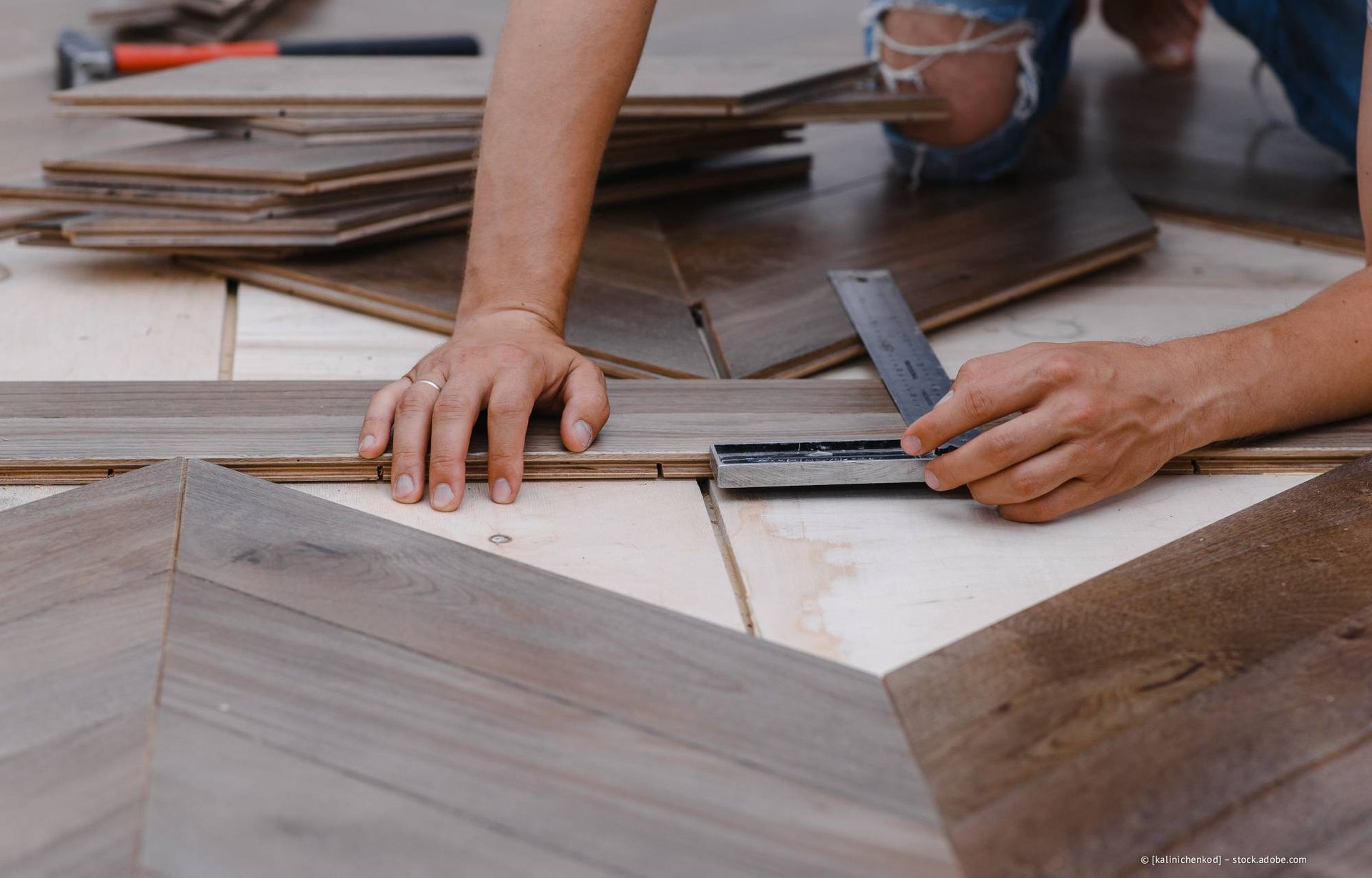 Eine Person verlegt Holzfußböden und benutzt dabei eine Wasserwaage.