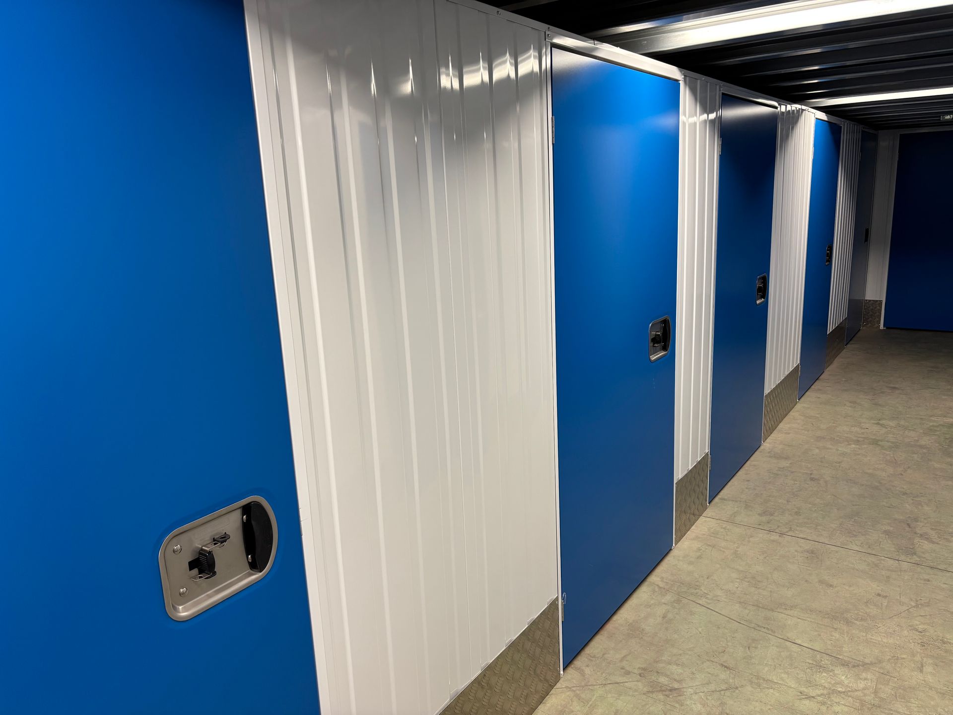 Couloir d'un box de stockage bleu avec portes blanches et sol en béton.