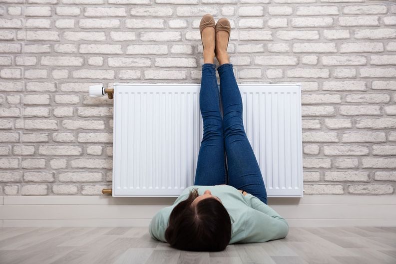Una mujer está tumbada en el suelo con las piernas levantadas delante de un radiador.