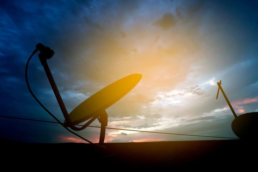 Una antena parabólica se recorta contra un cielo nublado al atardecer.
