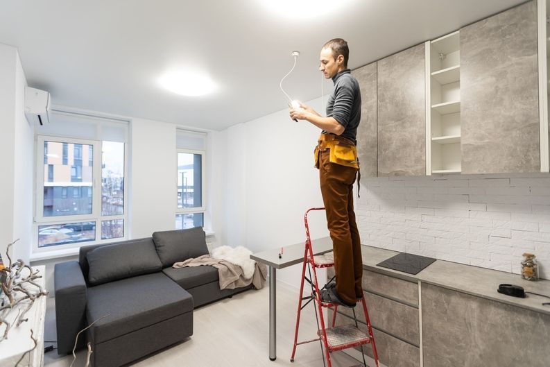 Un hombre está parado en una escalera en una sala de estar arreglando una lámpara.