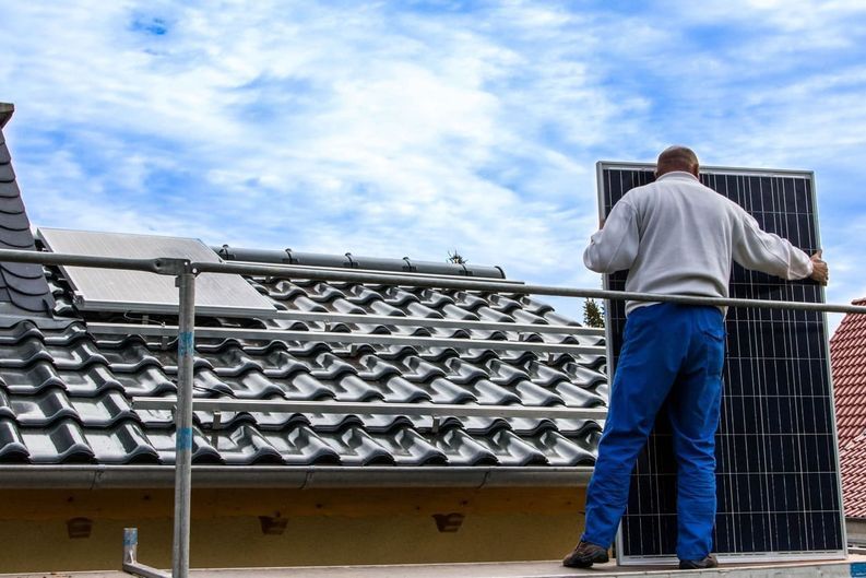 Un hombre está instalando paneles solares en el techo de una casa.
