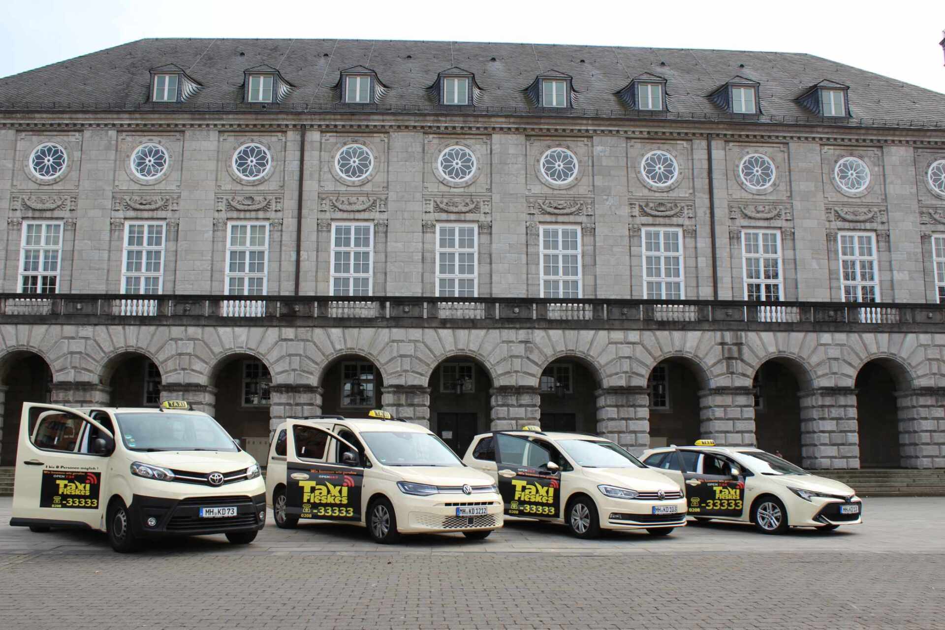 Vier Taxis parkten vor einem großen, reich verzierten Gebäude mit einer Kolonnade.