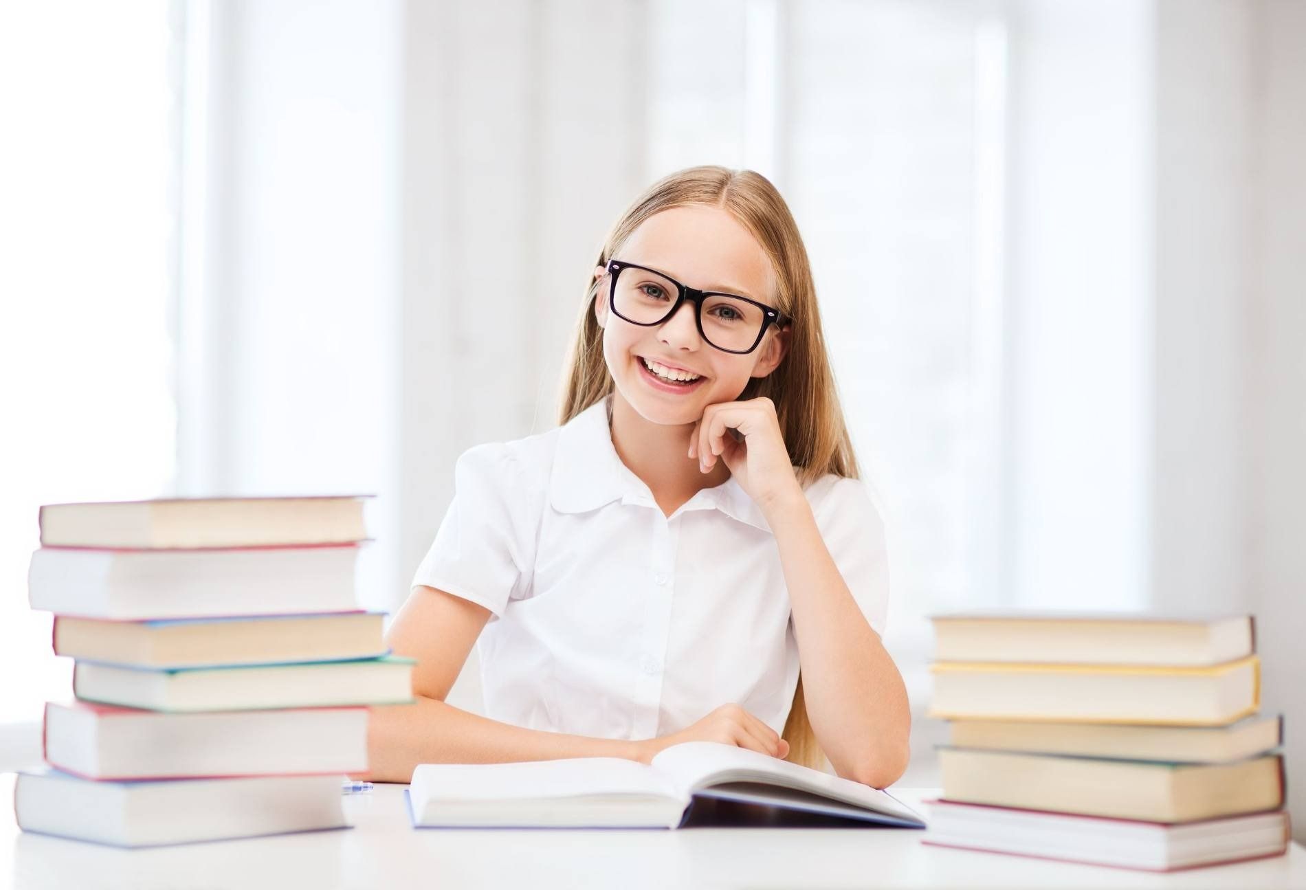 Una niña está sentada en una mesa con una pila de libros.
