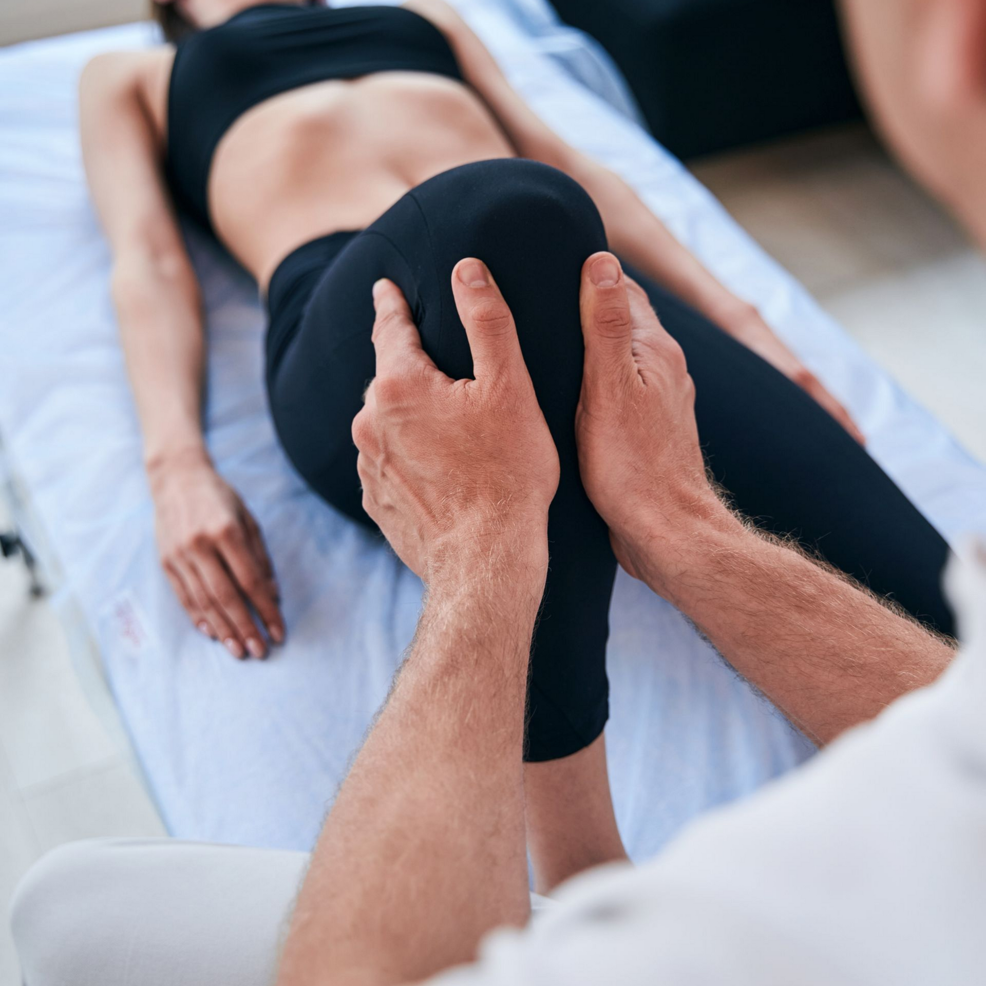 Des mains manipulent le genou d'un patient pendant une séance de physiothérapie sur une table de traitement.