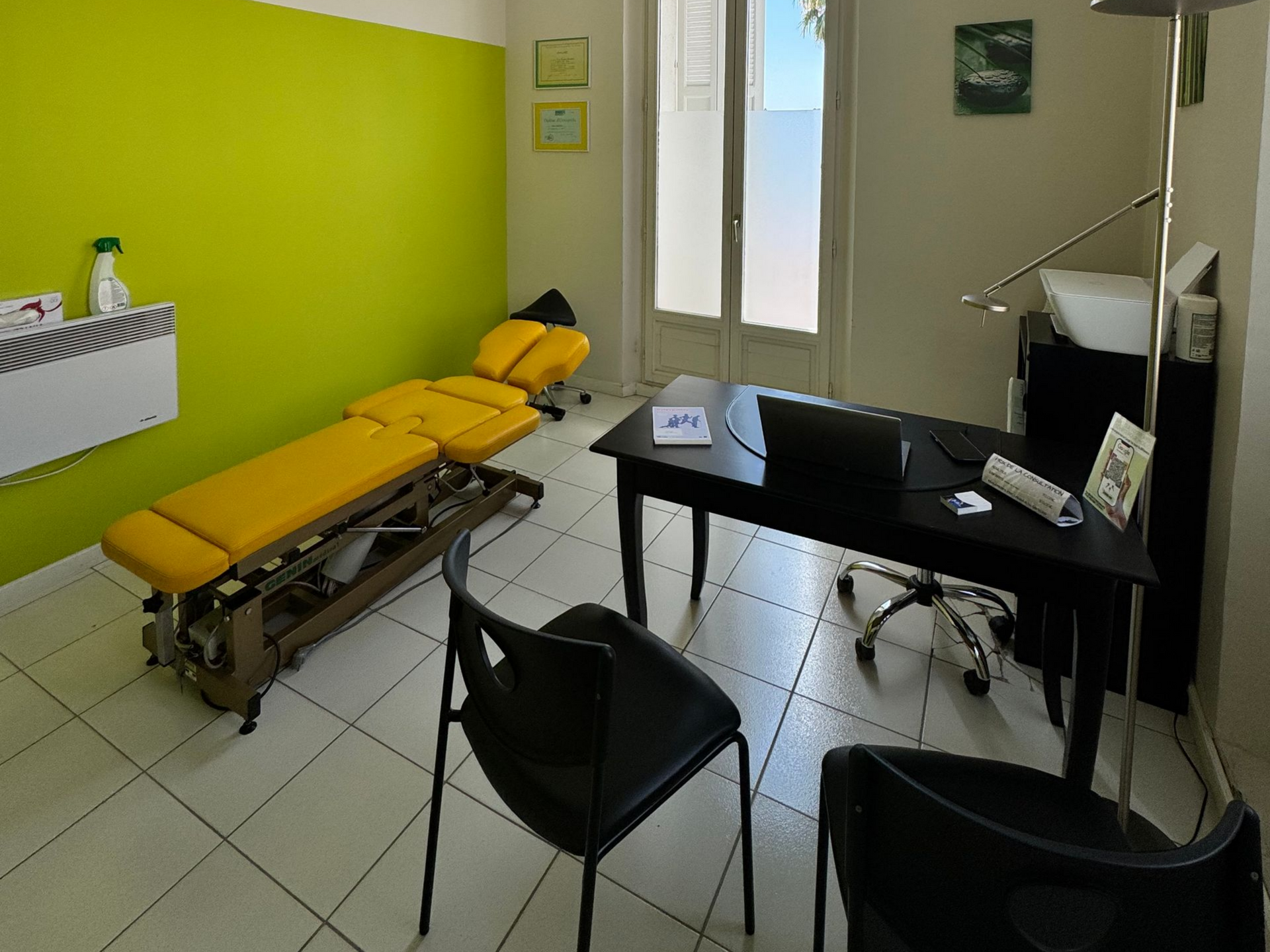 Cabinet de chiropracteur : table de traitement jaune, bureau noir avec ordinateur portable, deux chaises noires, mur vert vif.
