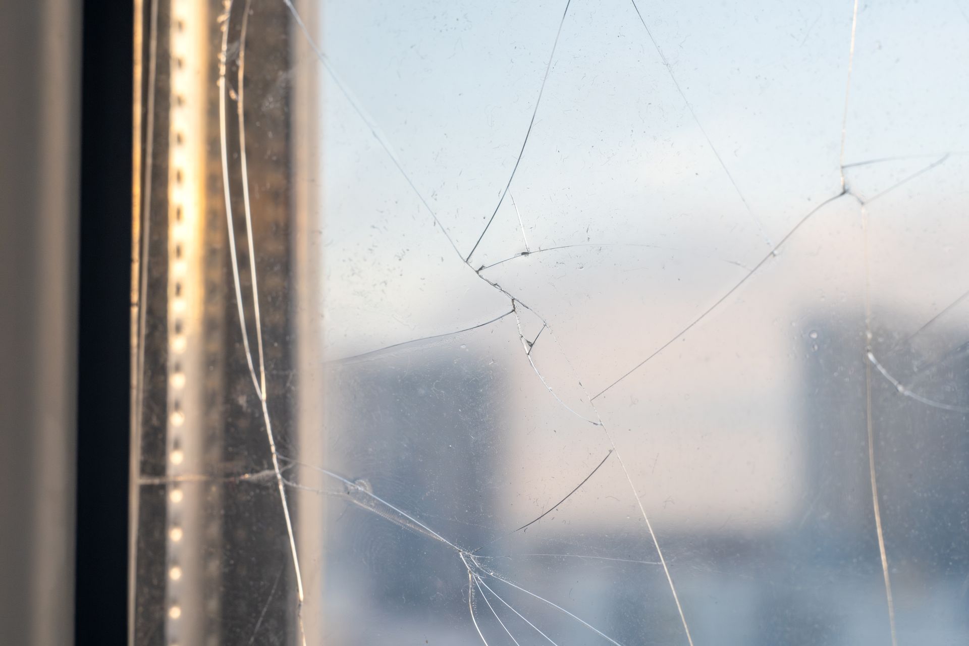Gros plan sur des fissures dans une vitre, avec une vue floue des immeubles de la ville en arrière-plan.