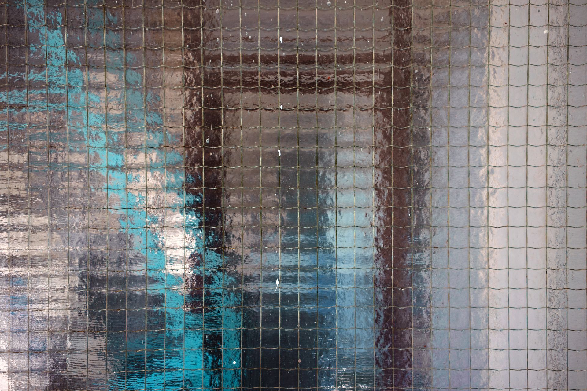 Gros plan à travers une vitre texturée à motif quadrillé, révélant un intérieur flou aux tons bleus et blancs.