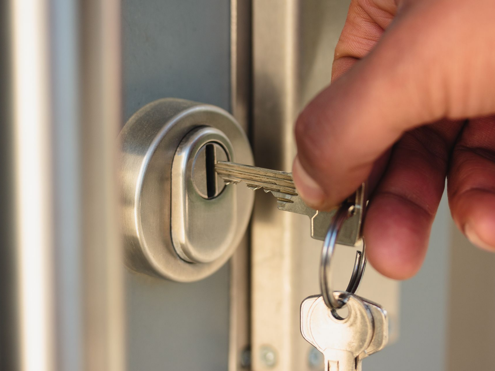 Une main tenant une clé et l'insérant dans une serrure de porte métallique.