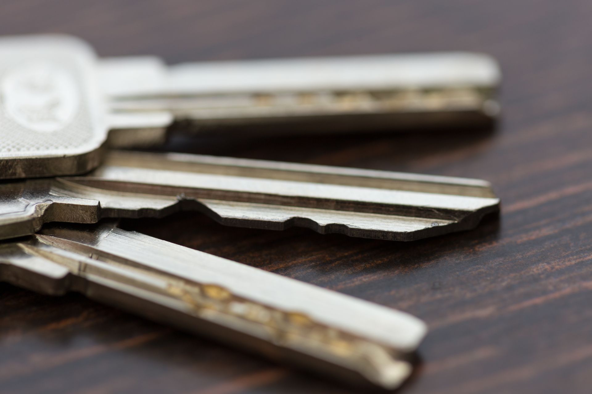 Gros plan sur trois clés argentées empilées les unes sur les autres sur une surface en bois brun foncé.