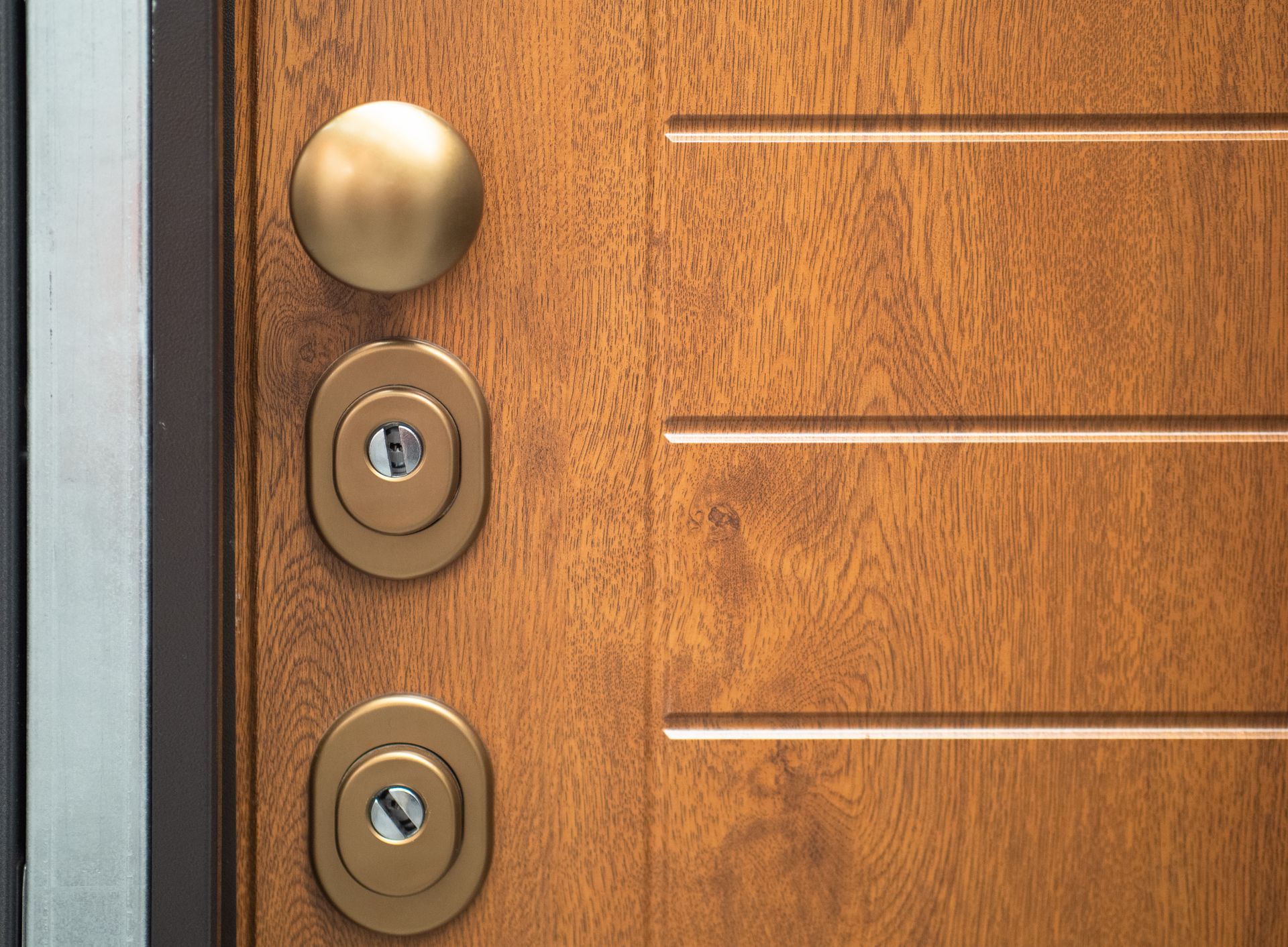 Gros plan sur une porte à l'aspect bois avec une poignée ronde et deux serrures à clé circulaires alignées verticalement, finition bronze métallisé.