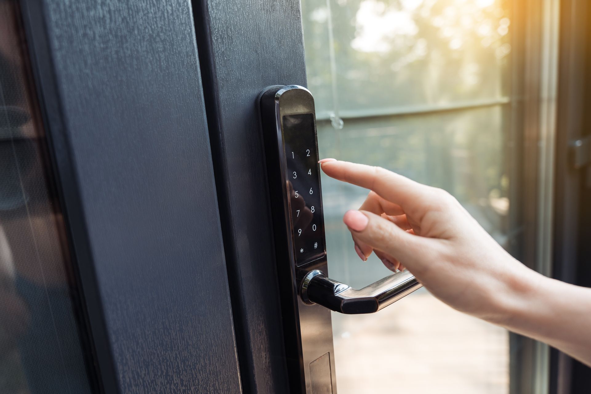 Une main compose un code sur un clavier électronique sombre fixé à une porte vitrée.