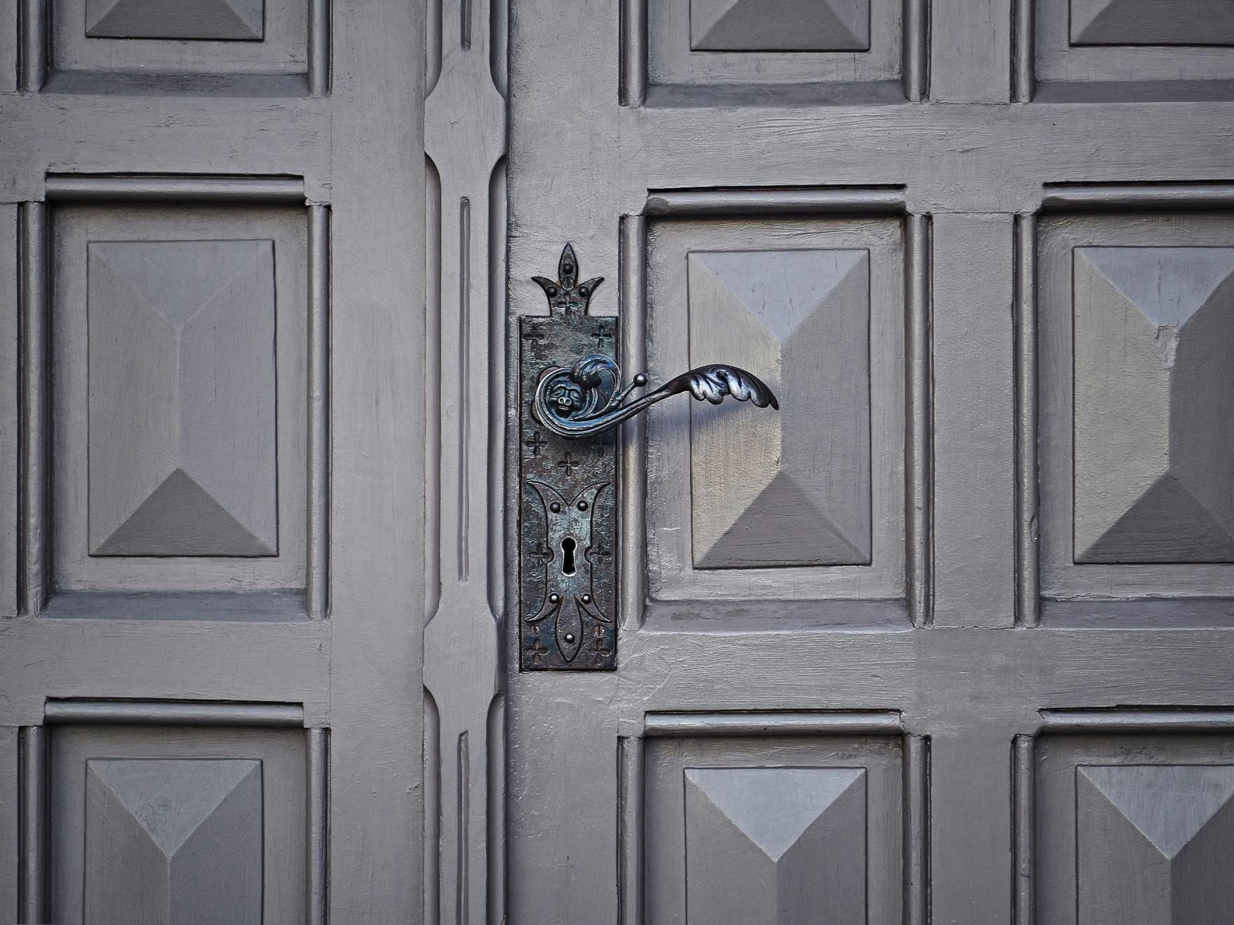 Gros plan sur une double porte grise à panneaux, ornée d'une poignée et d'une plaque de serrure en métal patiné.