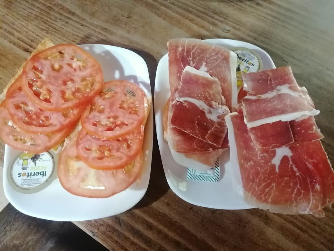 Dos platos de comida con tomates y jamón sobre una mesa de madera.