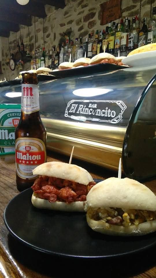 Hay dos sándwiches en un plato negro al lado de una botella de cerveza.