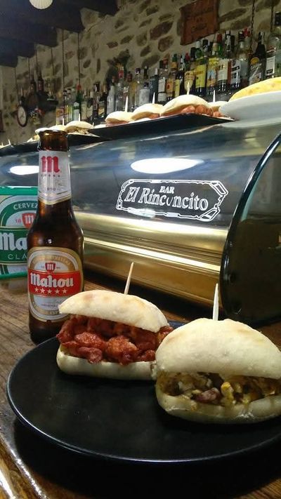 Hay dos sándwiches en un plato negro al lado de una botella de cerveza.