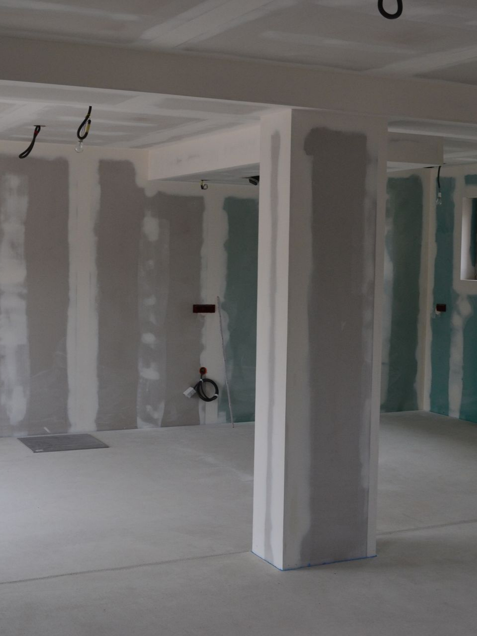 Intérieur en travaux, montrant les plaques de plâtre sur les murs, le plafond et les piliers de soutien.