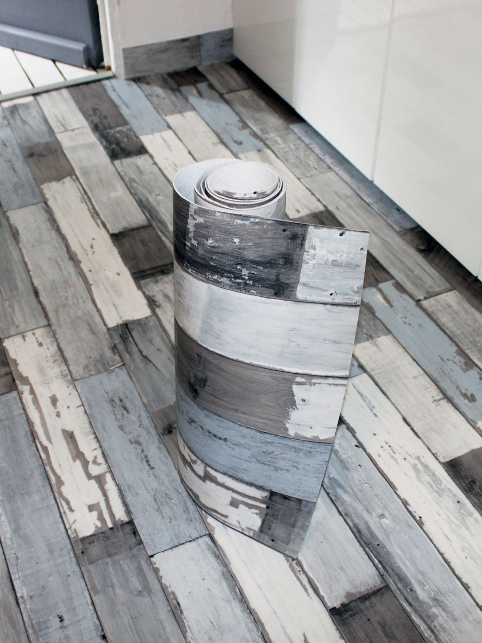 Rouleau de revêtement de sol en vinyle imitation bois vieilli sur un sol assorti.