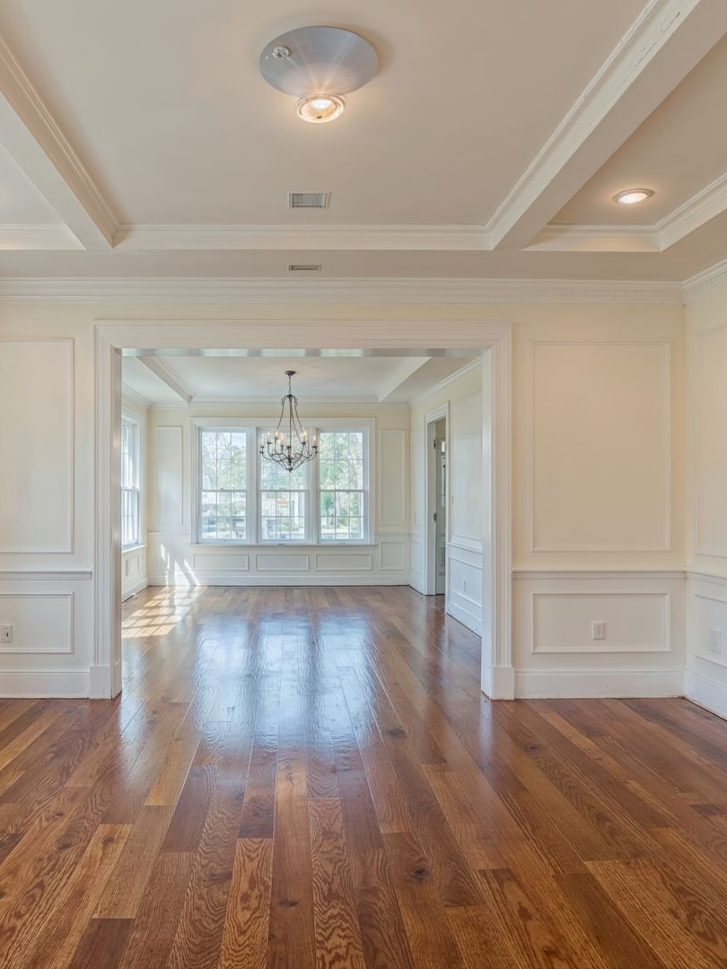 Pièce vide avec parquet, murs blancs et moulures, donnant sur un espace lumineux grâce à ses fenêtres.