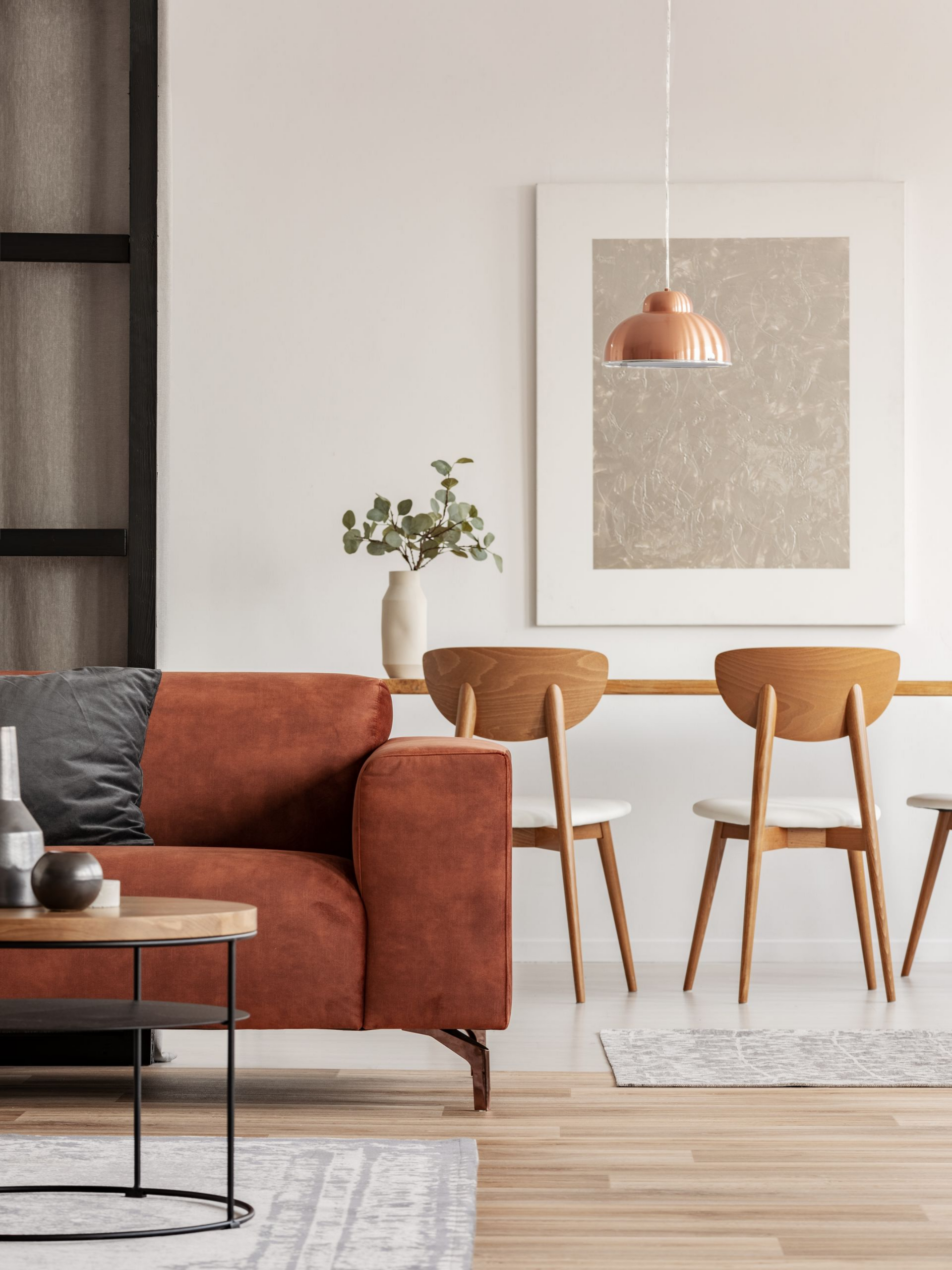 Canapé couleur rouille et table en bois avec chaises dans un espace de vie minimaliste et lumineux.