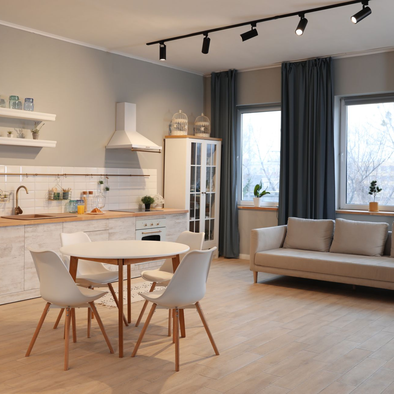 Cuisine-séjour moderne avec parquet clair, une table à manger ronde avec quatre chaises et un canapé beige.