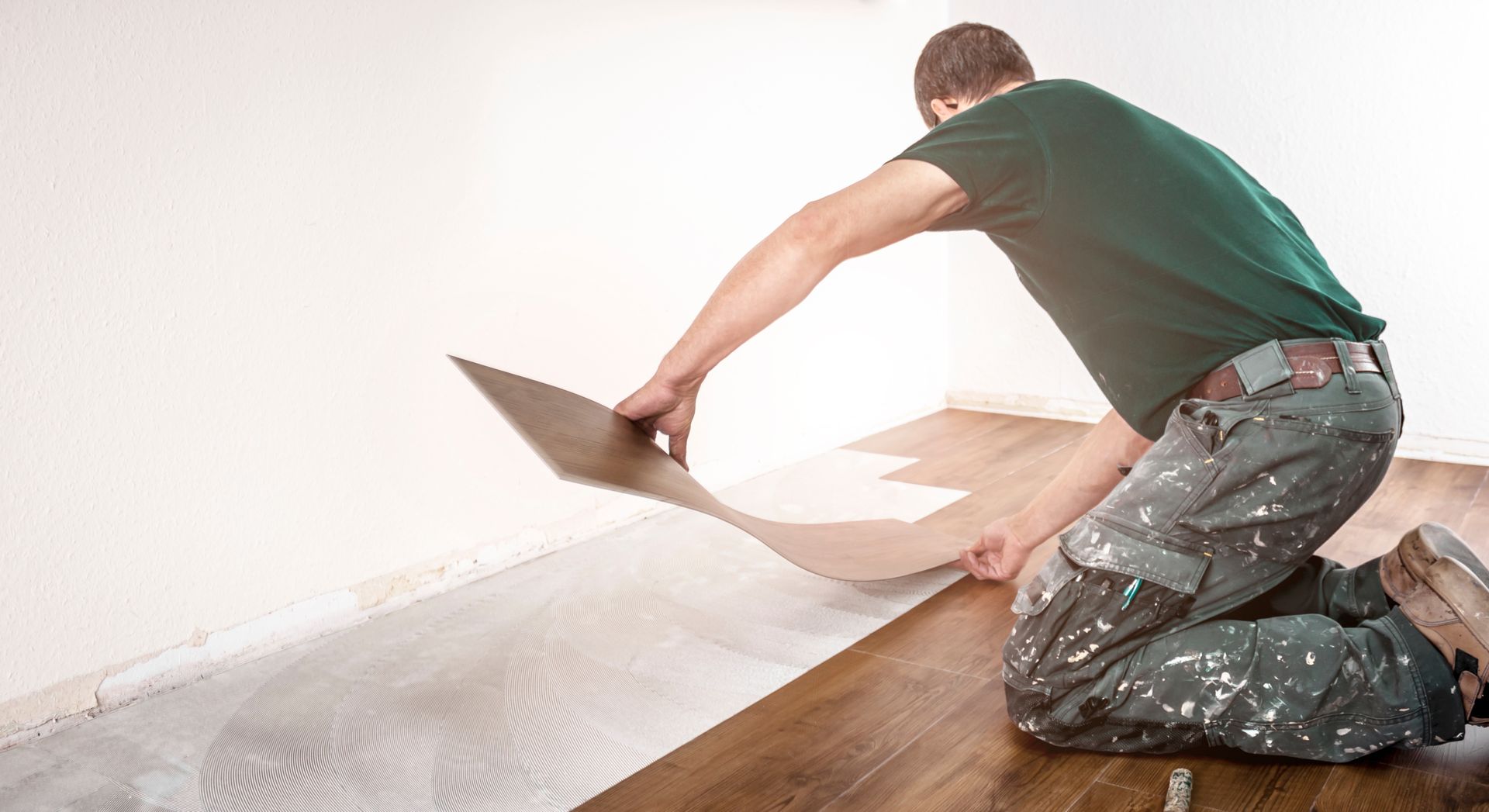 Un homme pose du parquet stratifié dans une pièce, agenouillé, tenant une lame.