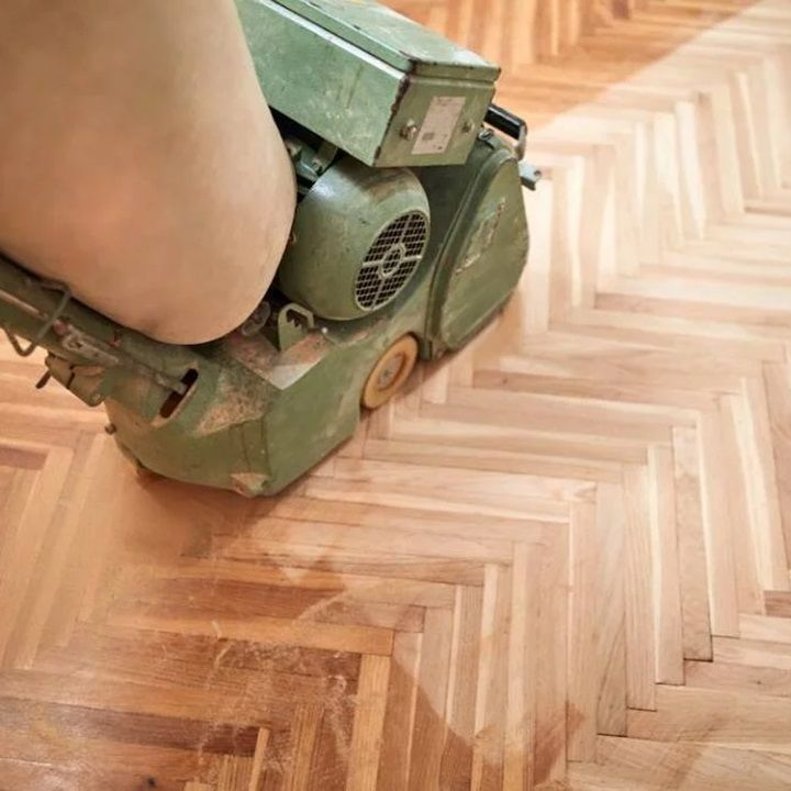 Ponceuse à parquet en train de rénover un plancher en bois à chevrons.