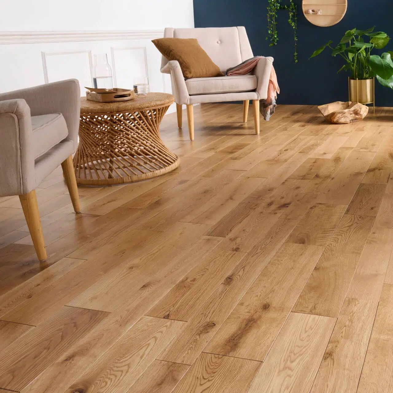 Sol en bois dans un salon, avec deux fauteuils beiges, une table basse en osier et des plantes.