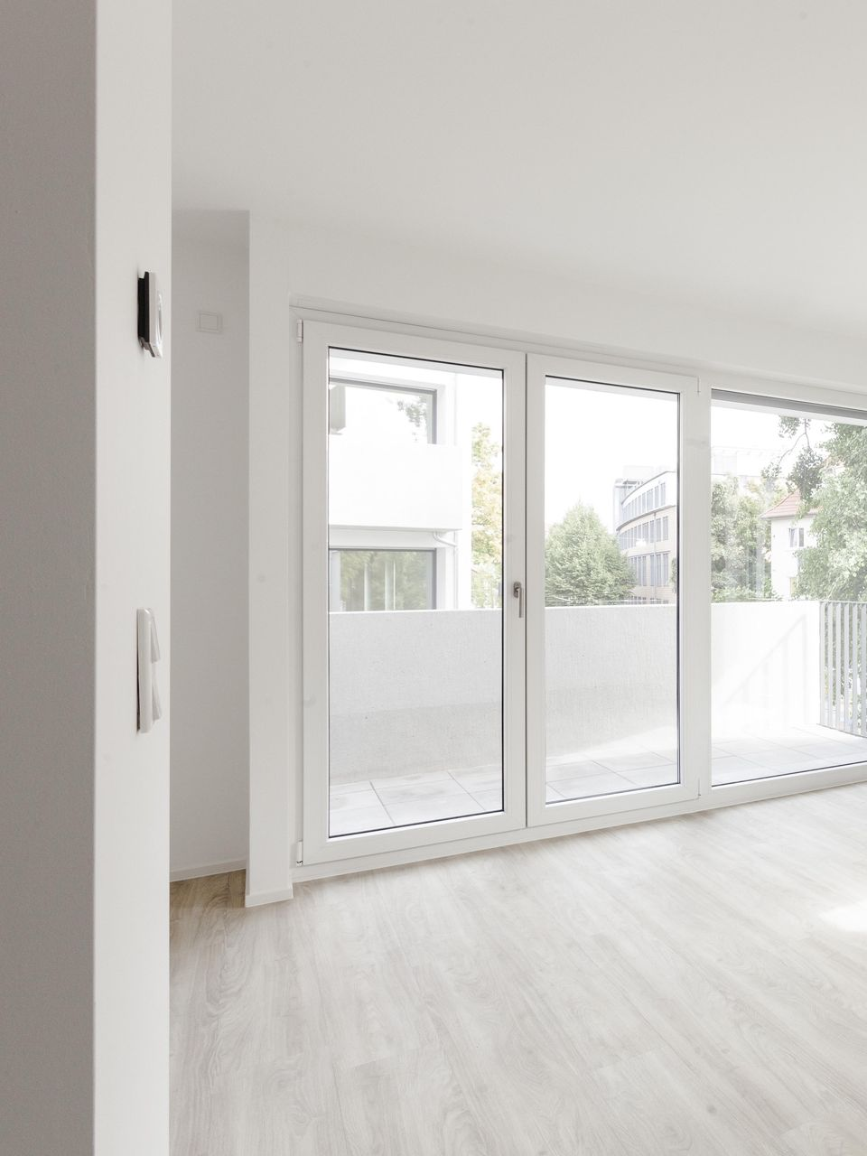Intérieur lumineux et épuré, avec des murs blancs, de grandes fenêtres et un parquet clair.