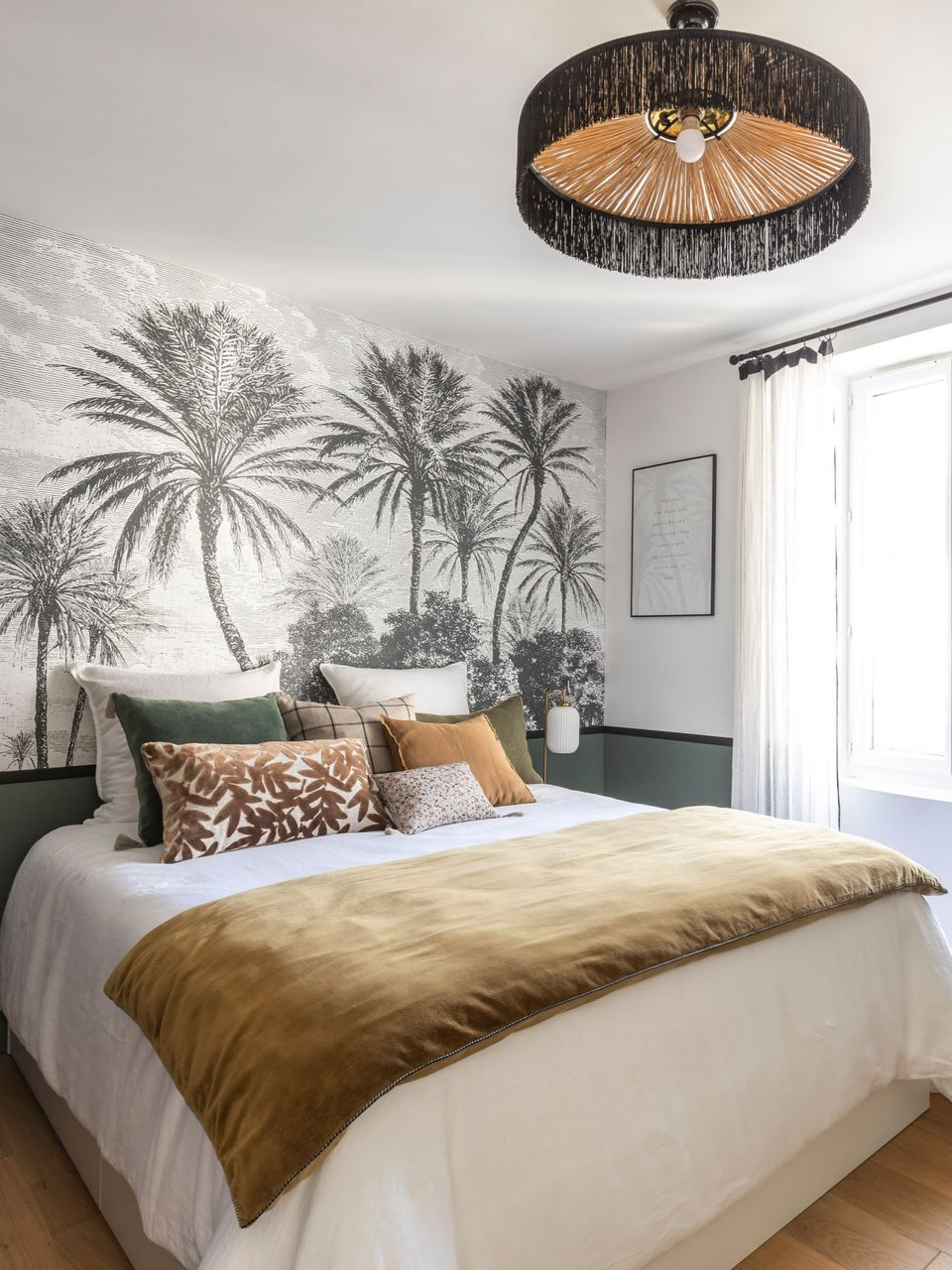 Chambre avec papier peint à motifs de palmiers, lit recouvert d'une couverture dorée et luminaire décoratif.