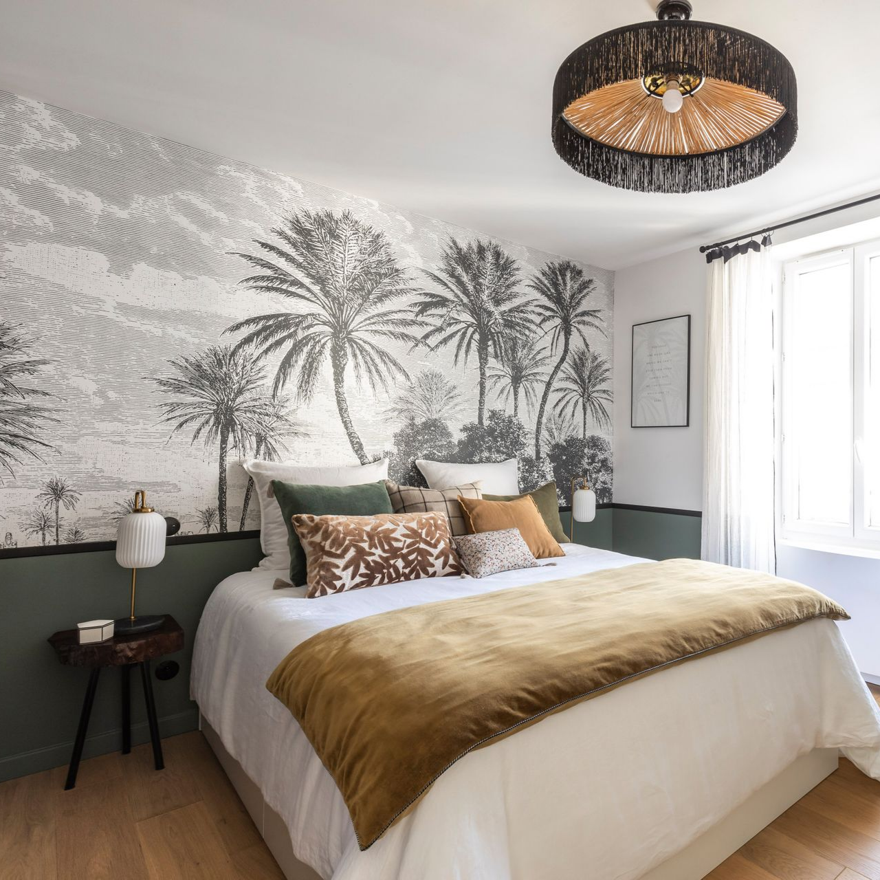 Chambre avec papier peint à motifs de palmiers, lit avec oreillers et suspension lumineuse en osier.
