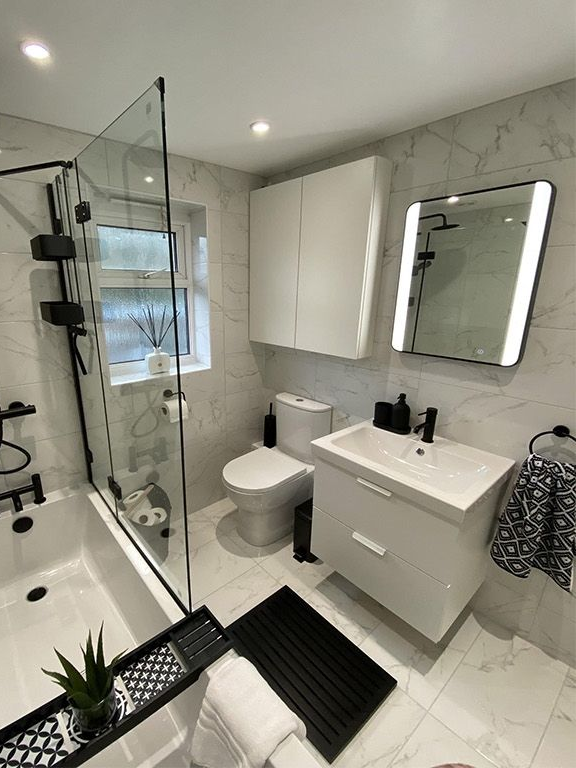 Salle de bains moderne blanche avec carrelage en marbre, robinetterie noire et paroi de douche en verre.