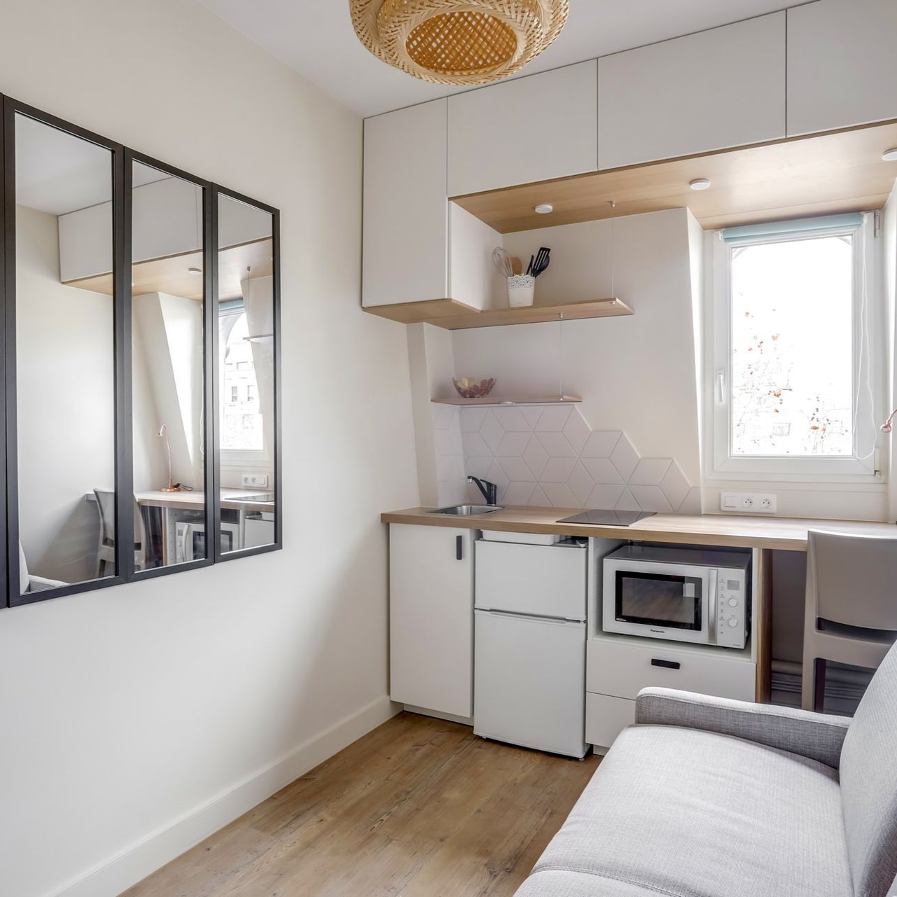 Petit studio avec kitchenette, bureau et canapé. Murs blancs lumineux, touches de bois et fenêtre.