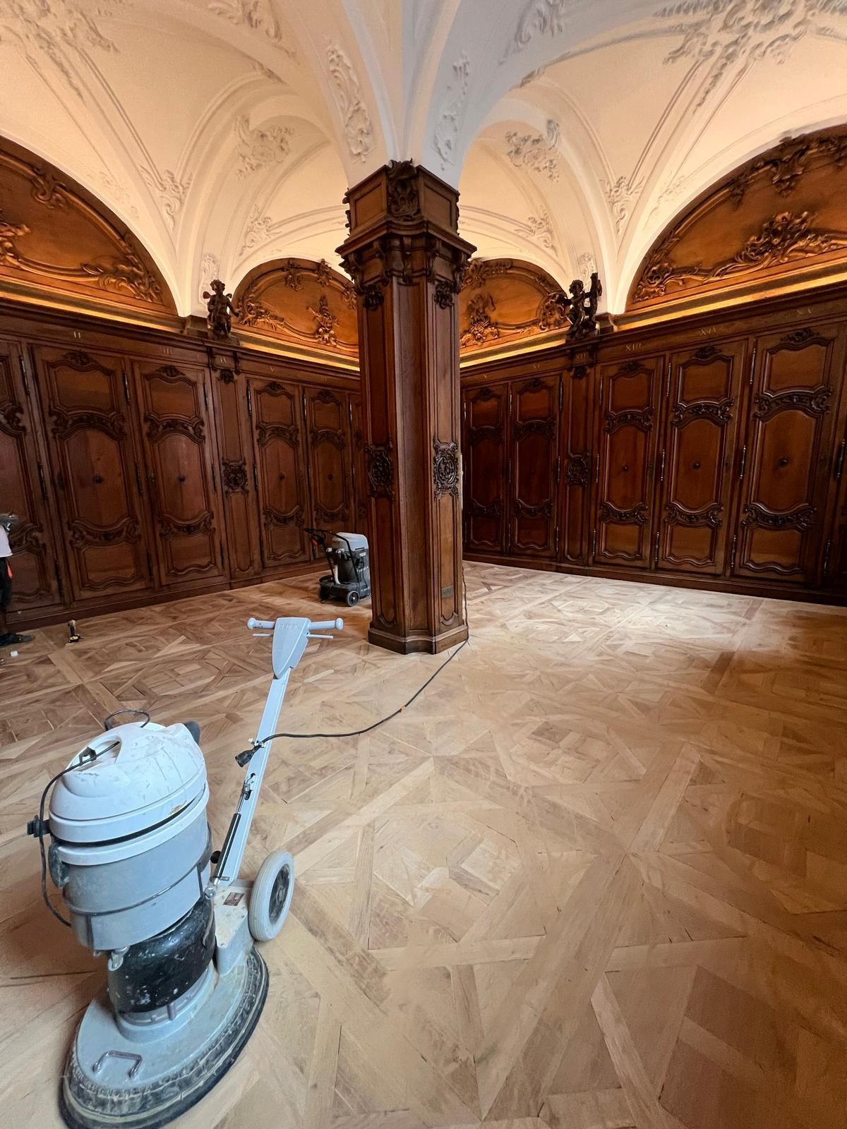 Ponceuse sur parquet clair dans une pièce avec lambris et détails de plafond ornementés.