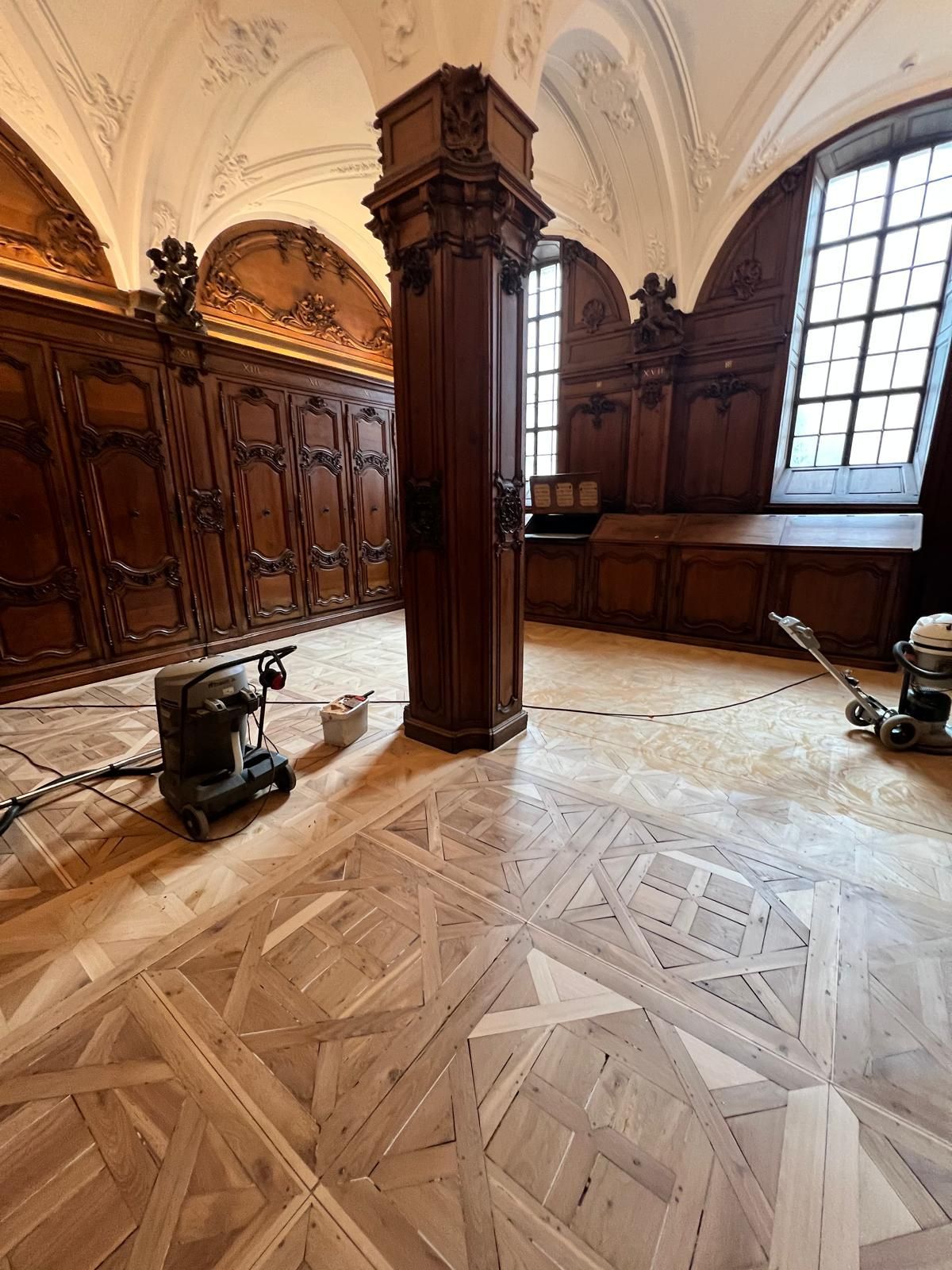Restauration d'un parquet en cours avec des ponceuses dans une pièce ornée de boiseries.