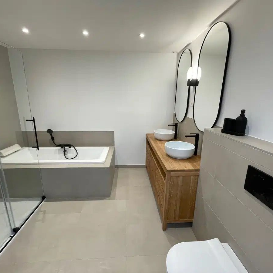 Salle de bains moderne avec baignoire, meuble de lavabo en bois à deux vasques et grands miroirs ovales.