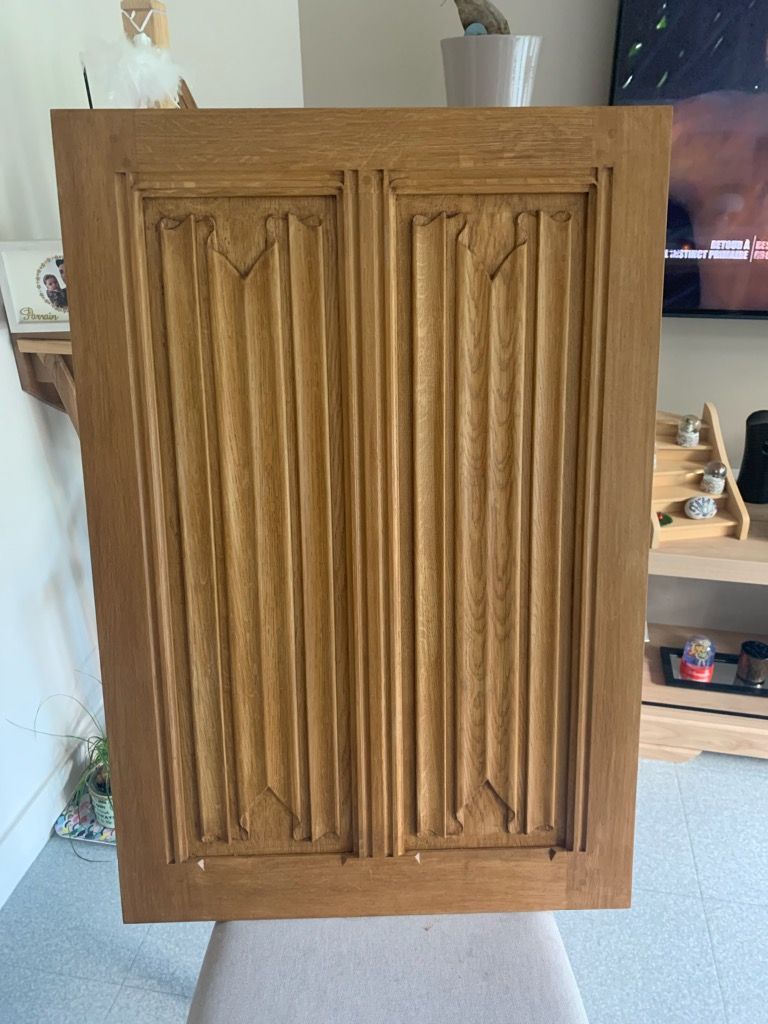 Porte d’armoire en bois à deux panneaux verticaux sculptés, centrée dans une pièce.