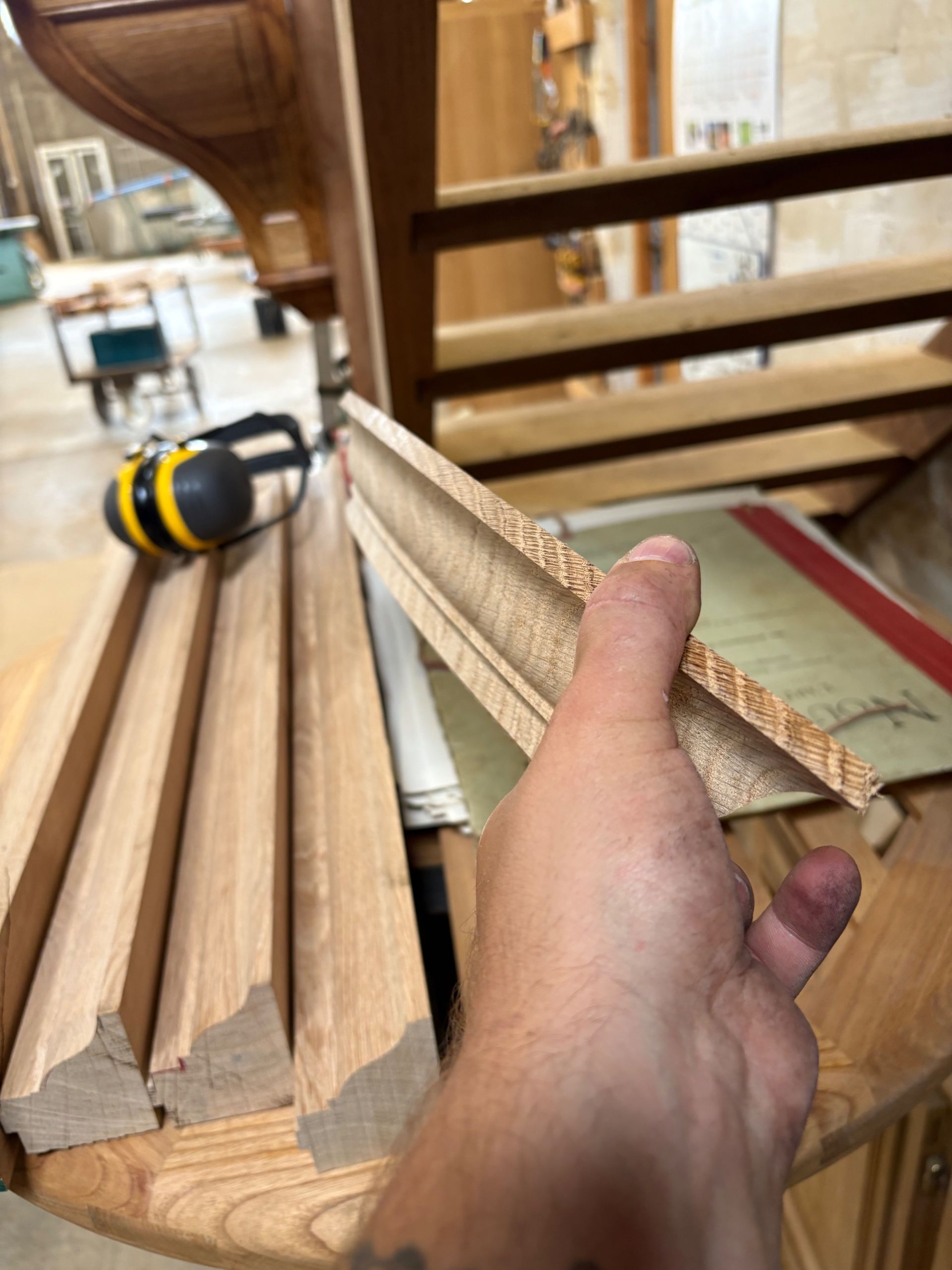 Une main tenant une pièce de moulure en bois à côté d’un tas de bois dans un atelier.