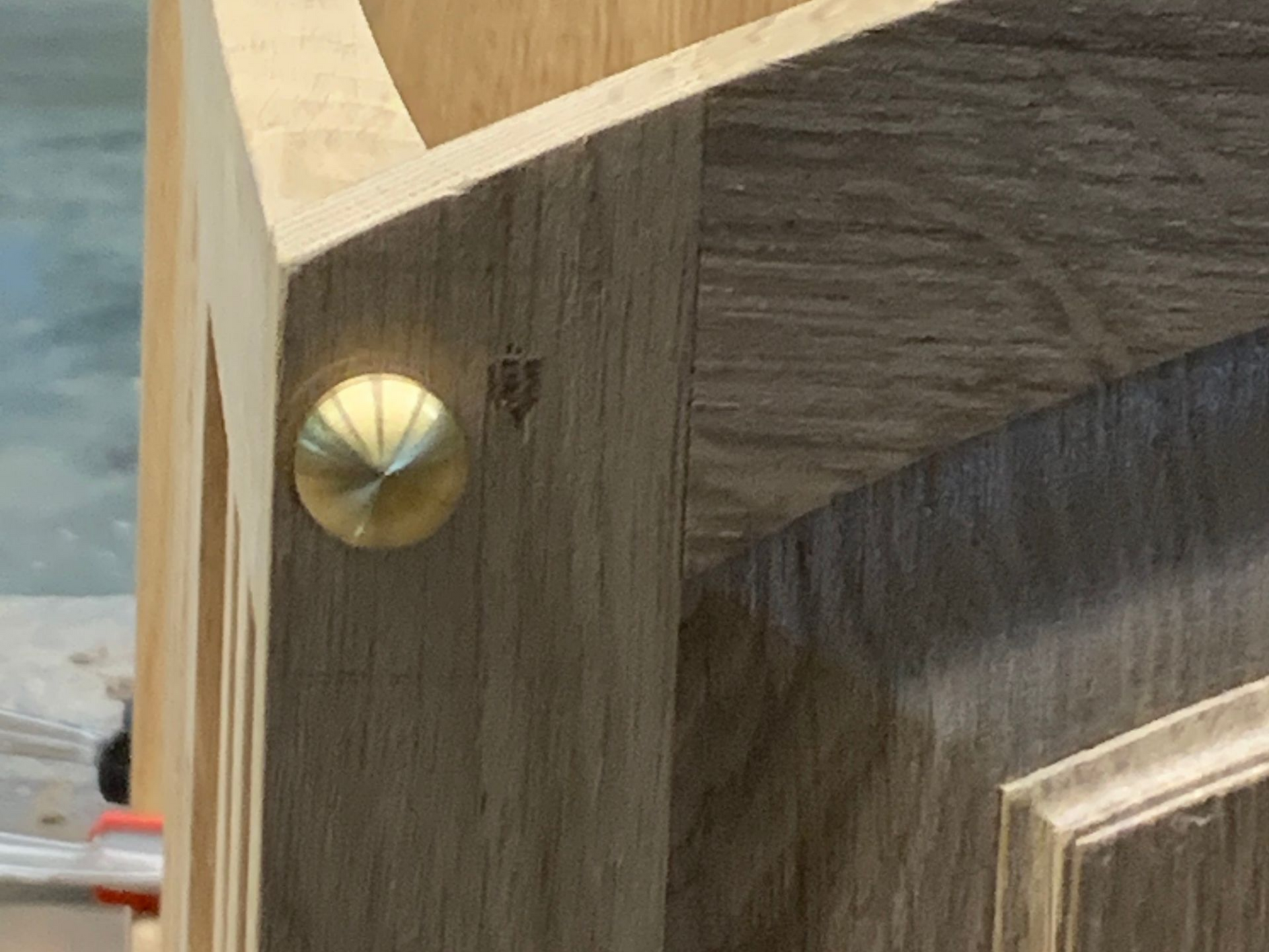 Gros plan sur un angle de meuble en bois avec un bouton en laiton et un veinage bien visible.