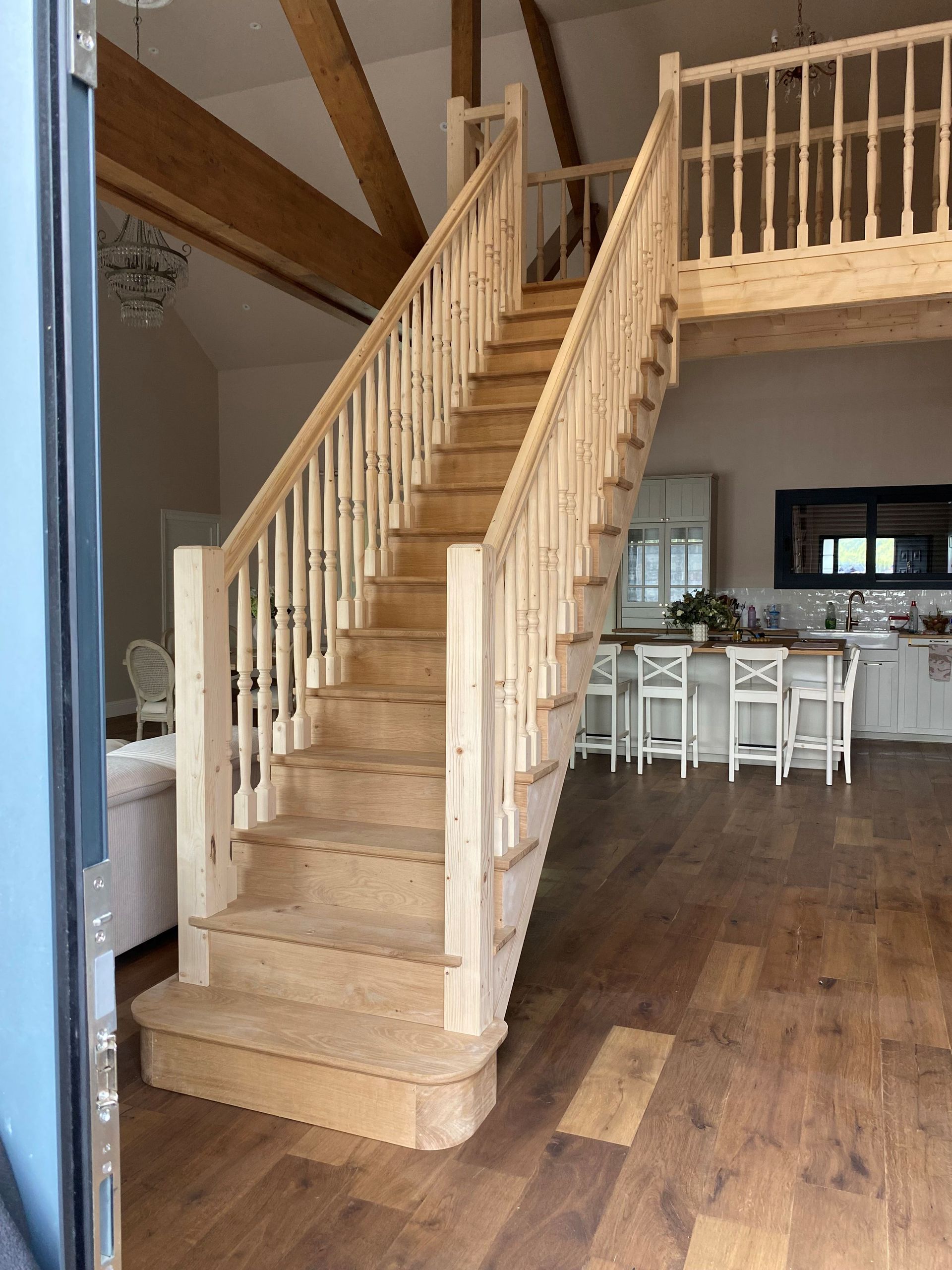 Escalier en bois dans un intérieur lumineux avec un espace salon et salle à manger ouvert.