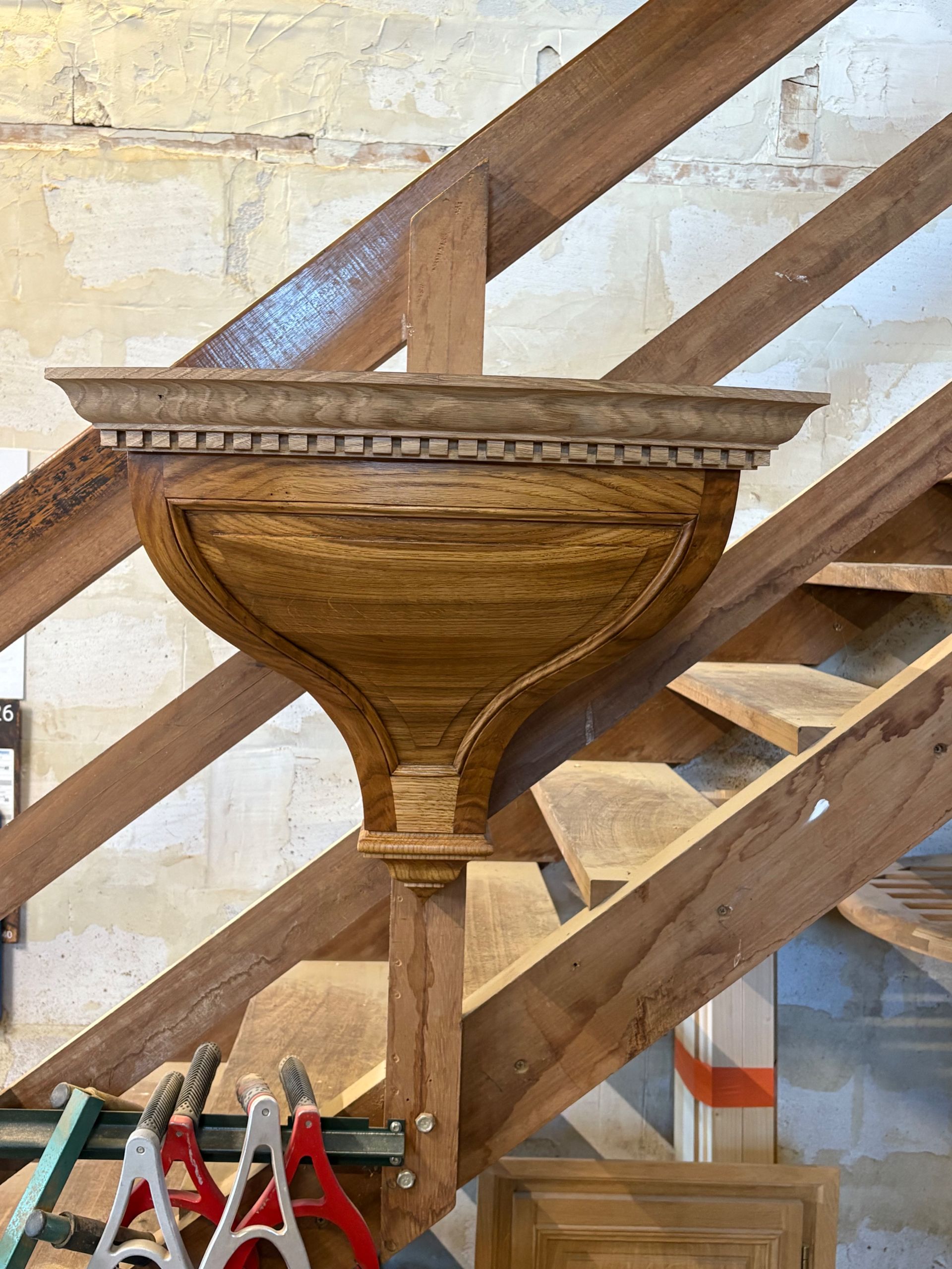 Fonts baptismaux en bois monté sur un support, devant un escalier.