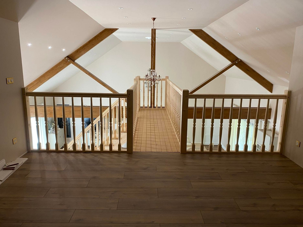 Palier supérieur avec des rampes en bois, des poutres apparentes et un lustre dans un espace mansardé lumineux.