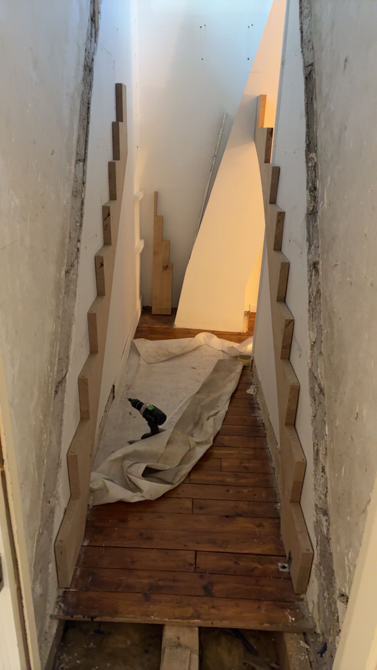 Couloir étroit avec des lames de plancher abîmées, des murs dont la peinture s’écaille et des débris de chantier sous un panneau incliné.