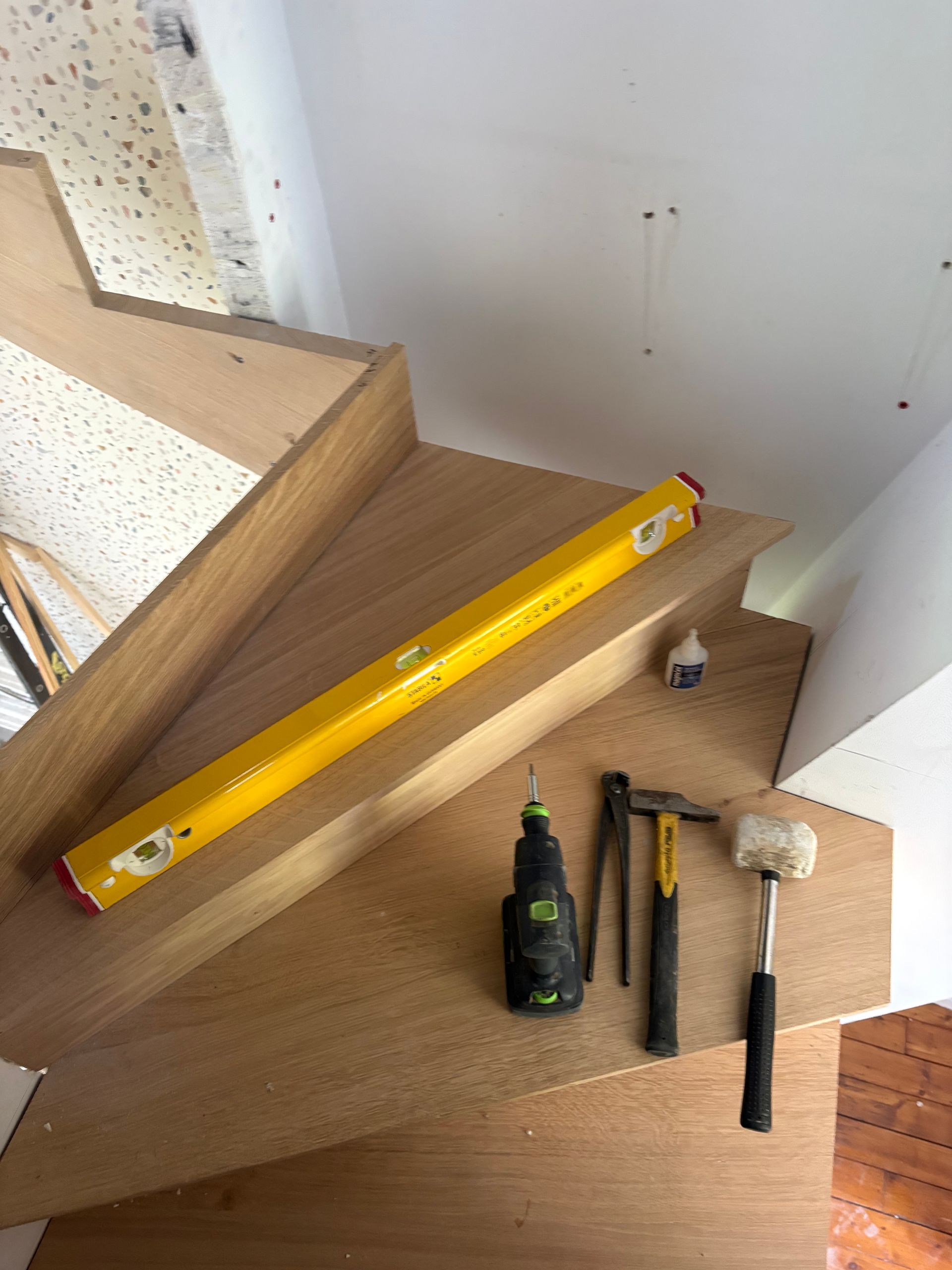 Niveau et outils à main sur le palier d’un escalier en bois pendant des travaux de rénovation.