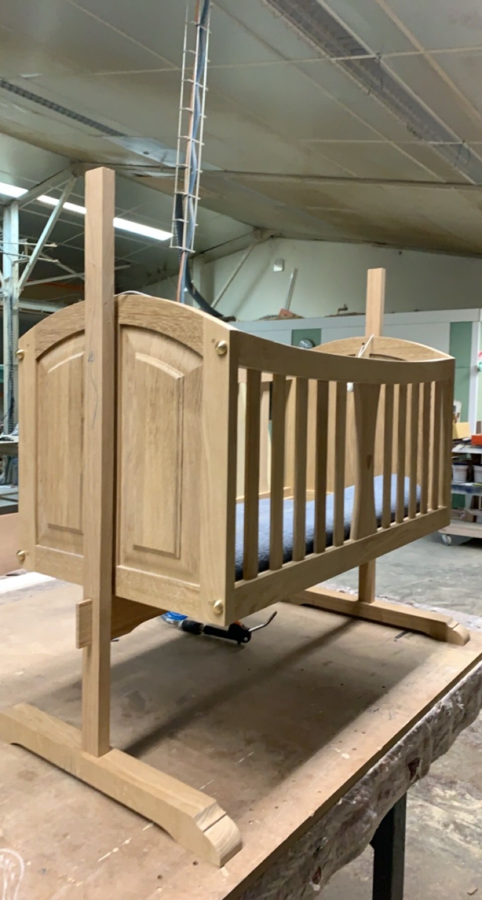 Prototype de lit bébé en bois sur une table d’atelier, avec un cadre brut et des côtés à barreaux.