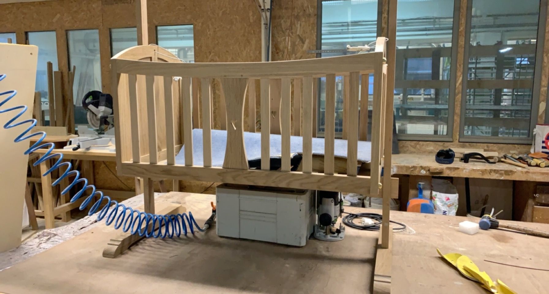 Cadre de berceau en bois posé sur un établi dans un atelier, avec des outils à proximité.