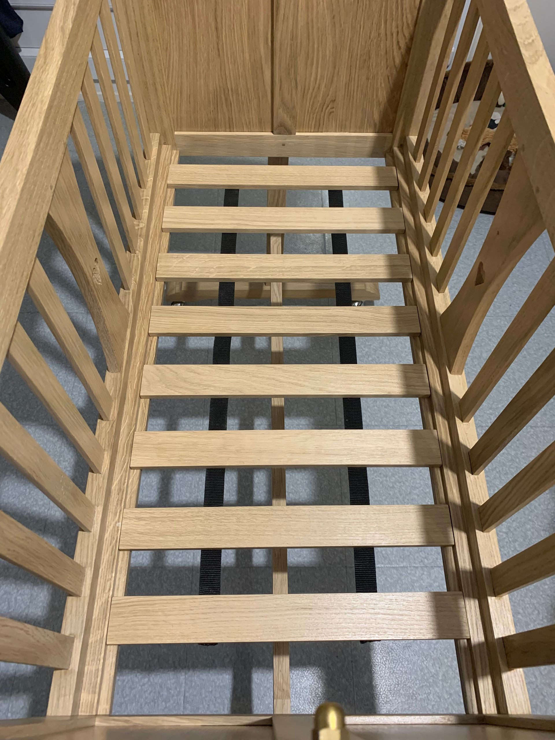 Lit bébé en bois avec côtés à barreaux et support de matelas, vu de dessus et de l’intérieur.