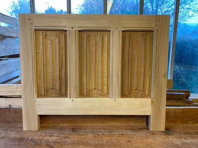Armoire en bois clair à trois portes à panneaux, posée sur une surface en bois devant une fenêtre.