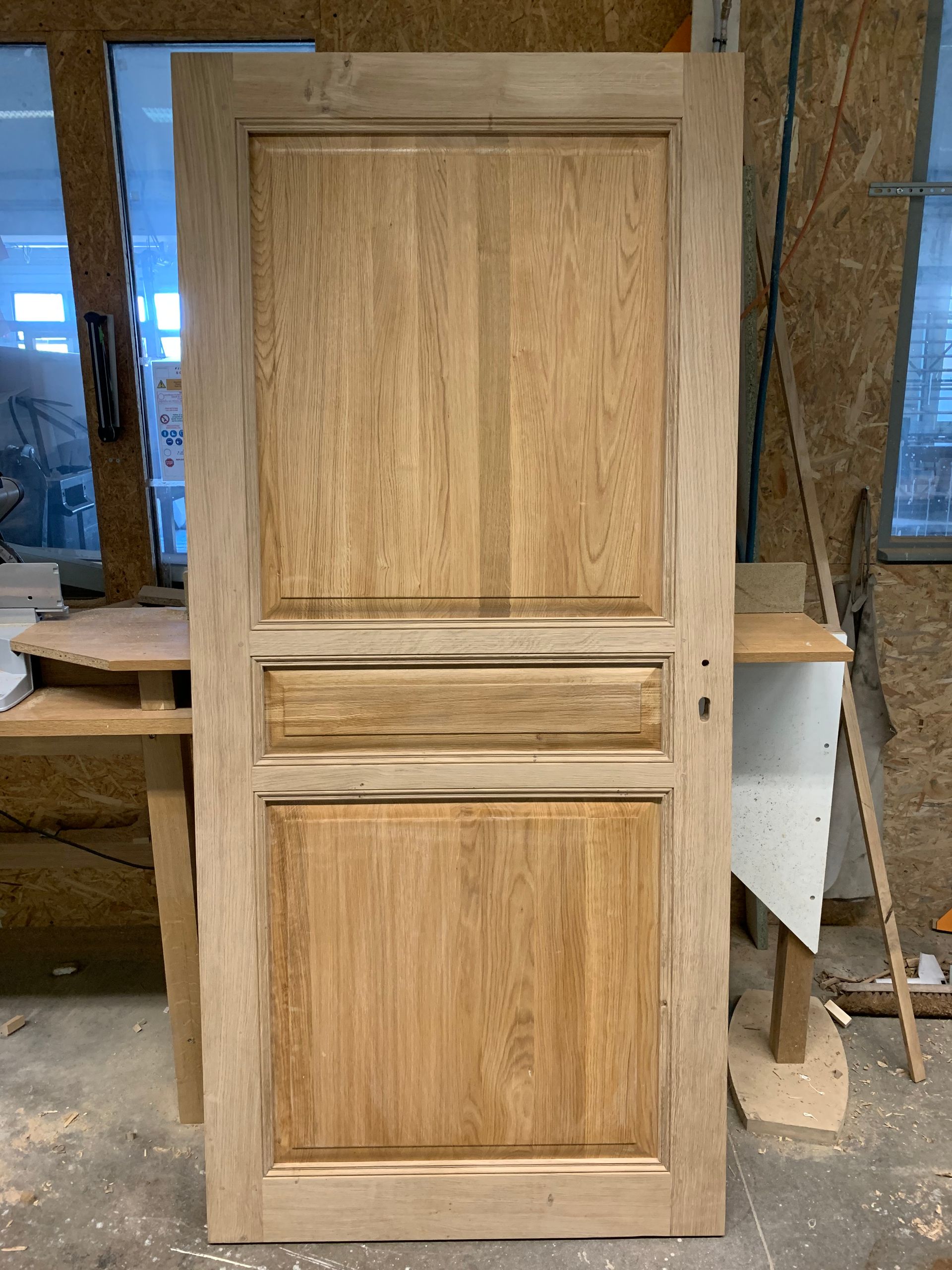 Porte d’armoire en bois brut à panneaux surélevés, dans un atelier.